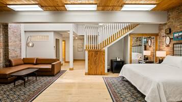 A spacious living area with a wooden ceiling, a staircase, a sofa, a bed, and a patterned rug.