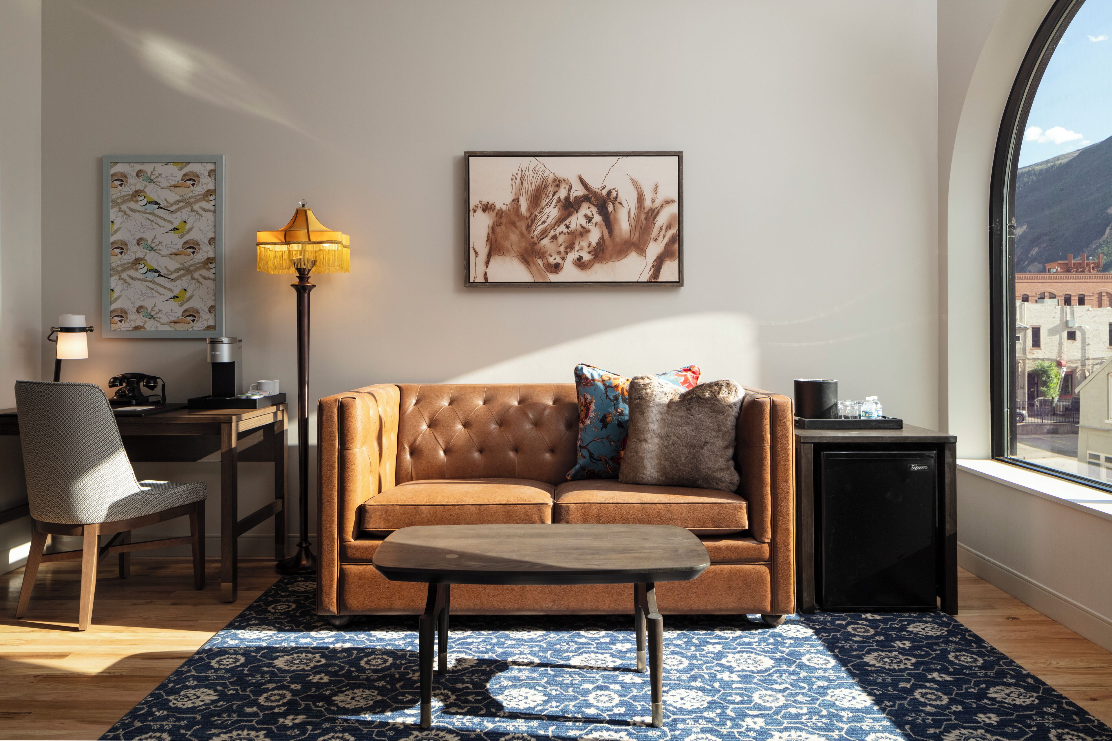 A modern living room with a brown sofa, a small table, a lamp, and a framed artwork on the wall.