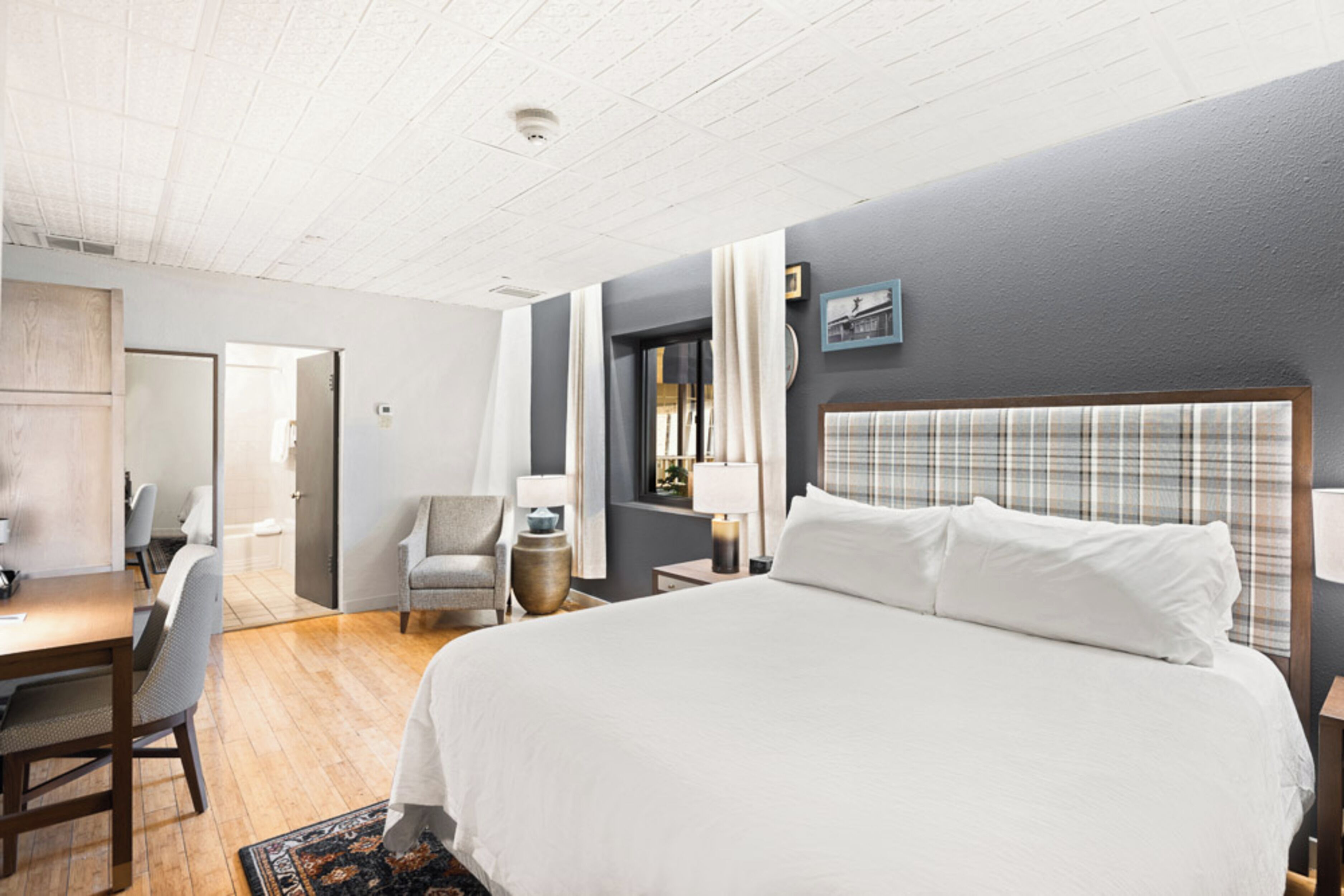 Una habitación de hotel con una cama grande, un escritorio, una silla y una ventana con cortinas.