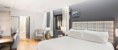 A hotel room with a large bed, a desk, a chair, and a window with curtains.