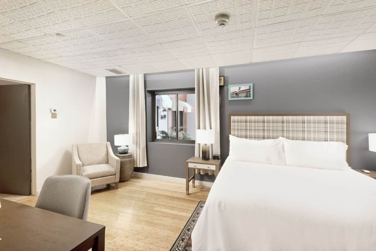 Una habitación de hotel con cama, una silla, una mesita y un ventanal con cortinas.