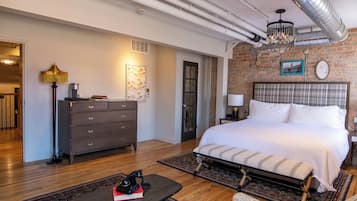 A modern bedroom with a large bed, a dresser, a desk with a lamp, and a chandelier.