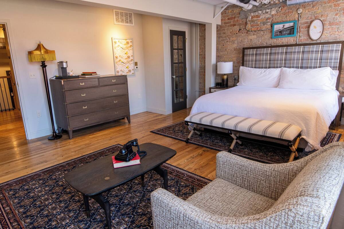 Un dormitorio con una cama, un aparador, una lámpara, una silla y una alfombra.