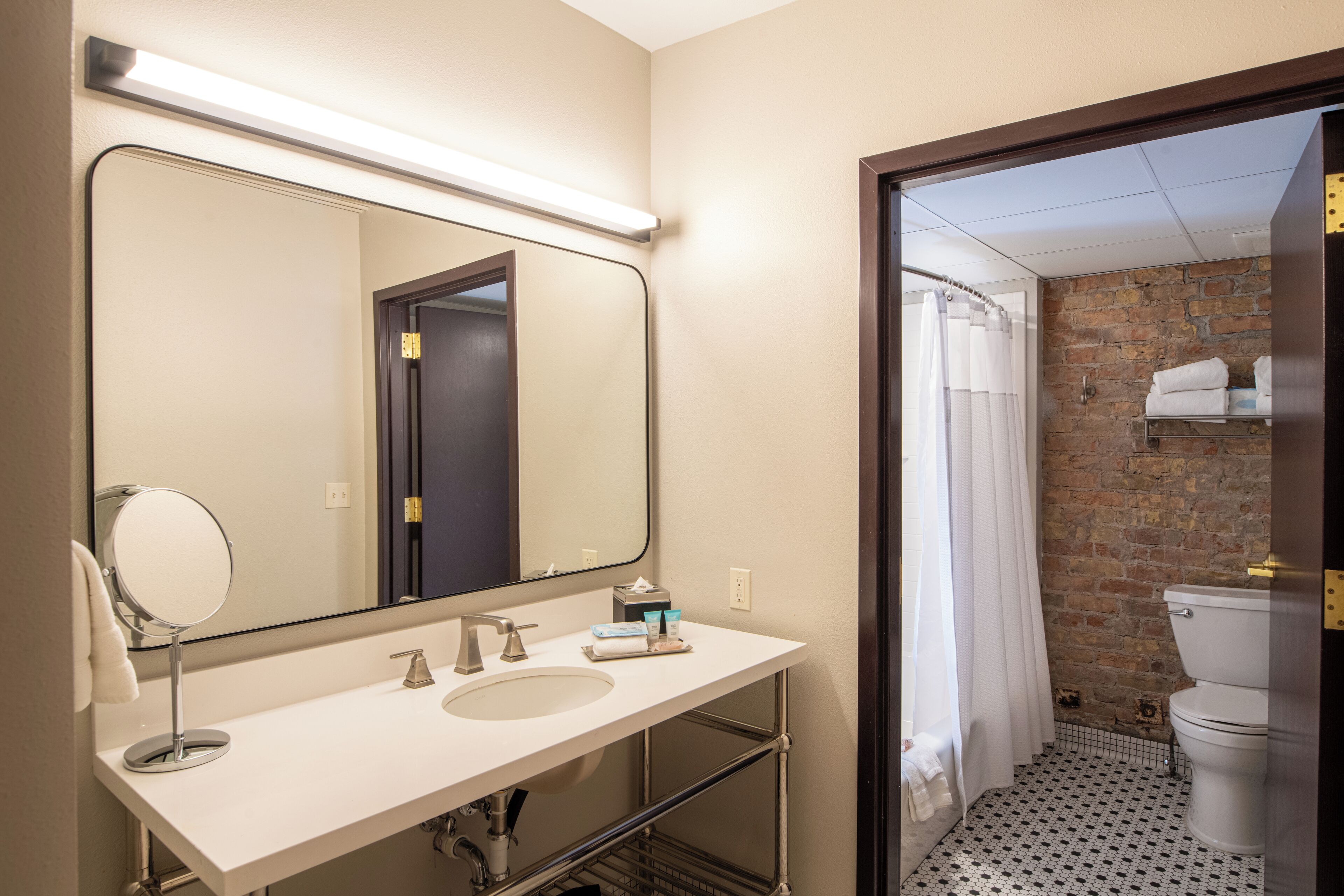 A bathroom with a white sink, a large mirror, and a shower area with a brick wall.
