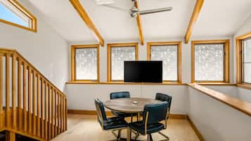 A room with a wooden ceiling, a ceiling fan, a round table with chairs, and large windows with frosted glass.
