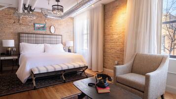 Un dormitorio con una cama grande, una silla, una mesa y una pared de ladrillo.