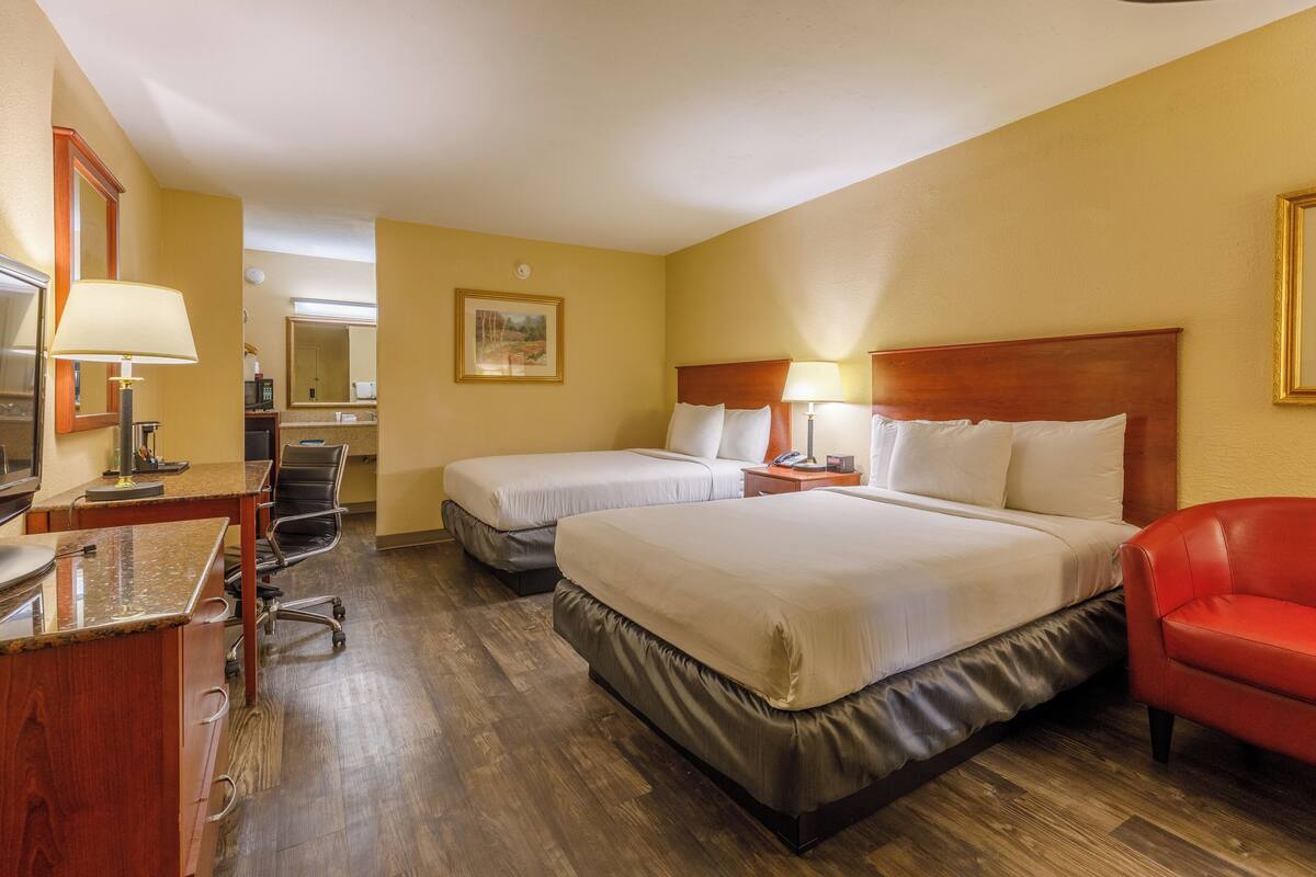 Une chambre d’hôtel avec deux lits, un bureau avec une lampe, une chaise et un canapé rouge.