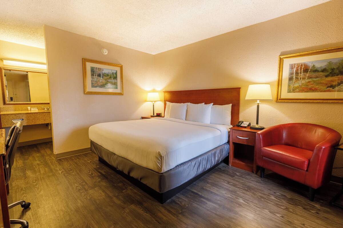 Une chambre d’hôtel avec un grand lit, des lampes de chevet, un fauteuil en cuir rouge, un bureau en bois et un tableau au mur.