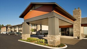 A modern hotel with a covered entrance, stone pillars, and a parking lot.