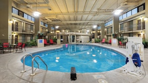 An indoor swimming pool with multiple levels of balconies, red chairs, and a lifeguard stand.