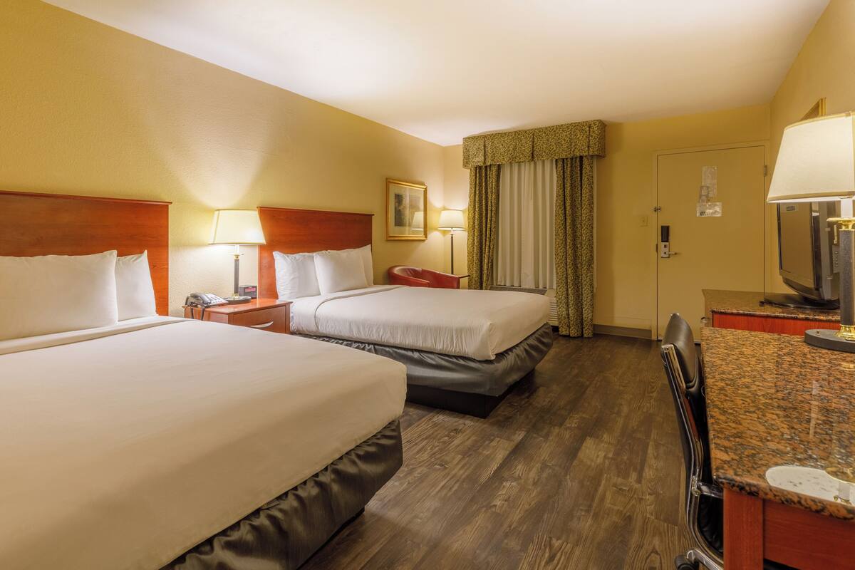 Une chambre d’hôtel avec deux lits, un bureau avec une chaise, une lampe, une télévision et une porte avec une serrure.