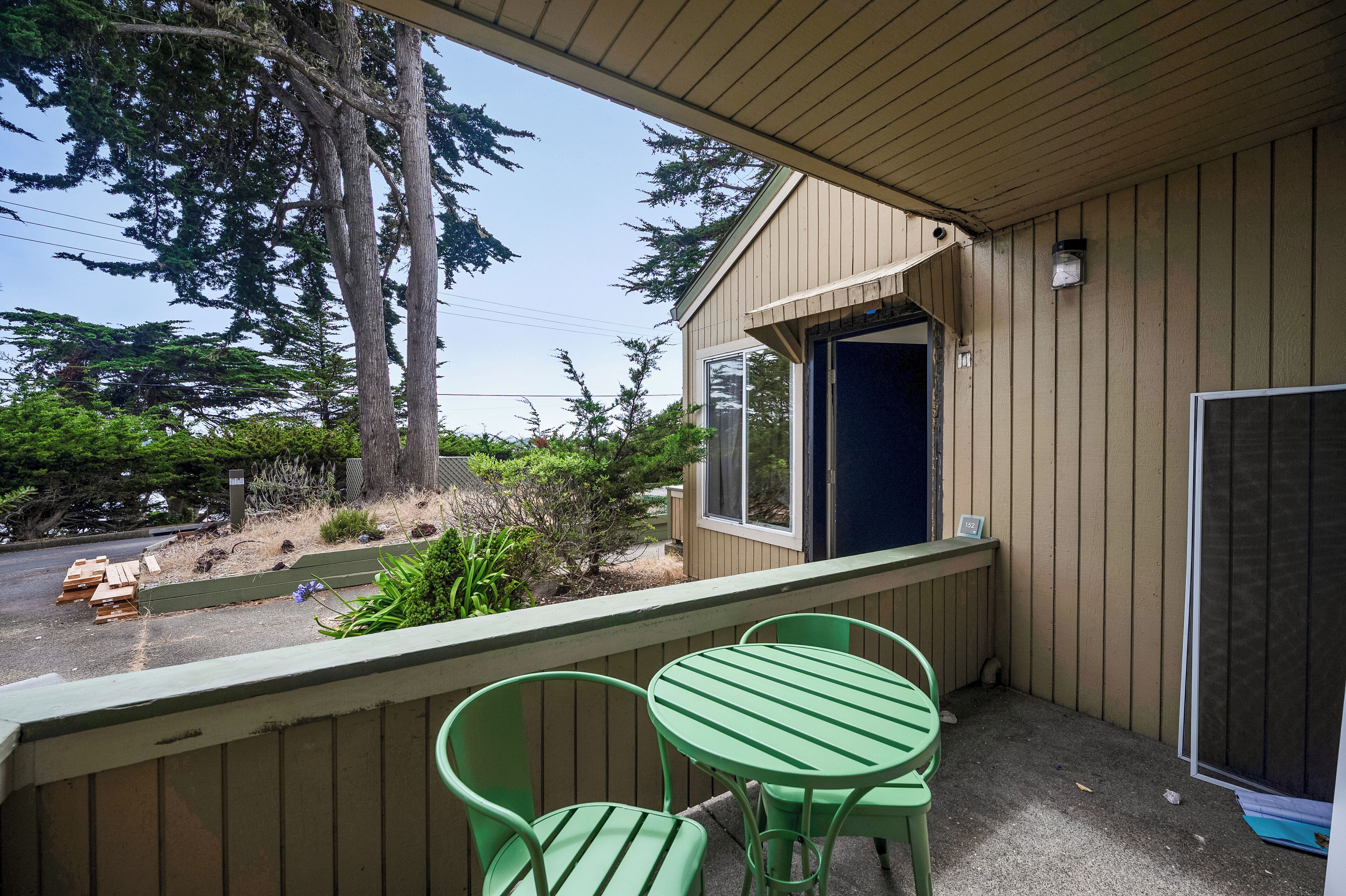 A covered outdoor area with a wooden deck, two green metal chairs, and a table.