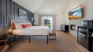 Ein modernes Schlafzimmer mit einem großen Bett, Nachttischen, einer Bank, einem Fernseher und einer Küchenzeile inklusive Kühlschrank.