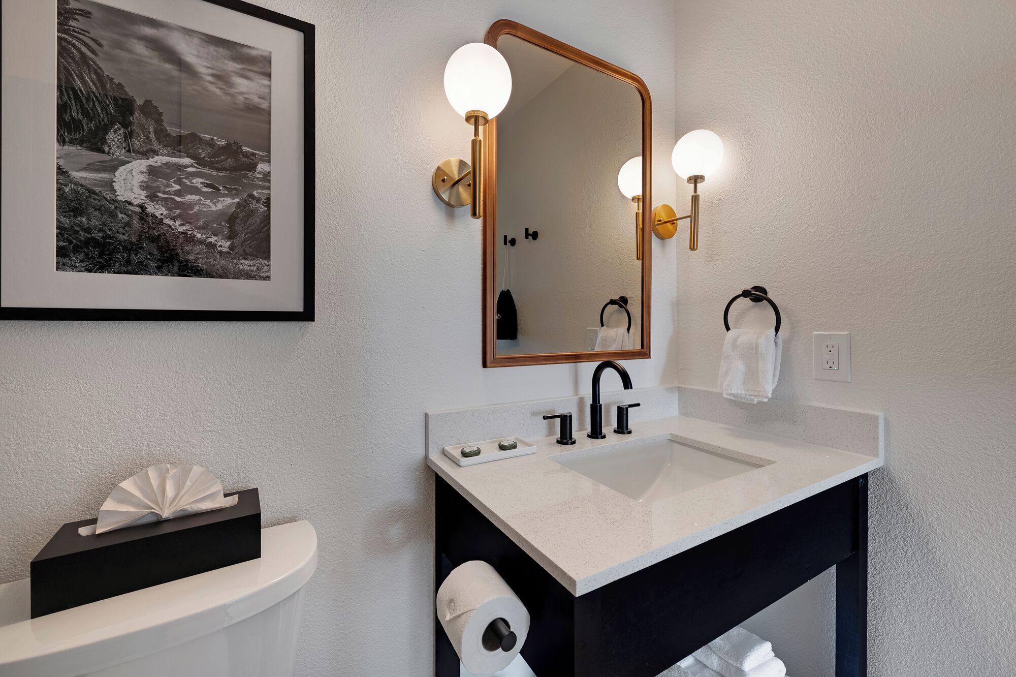 A modern bathroom with a white sink, black vanity, and a framed black and white photograph on the wall.