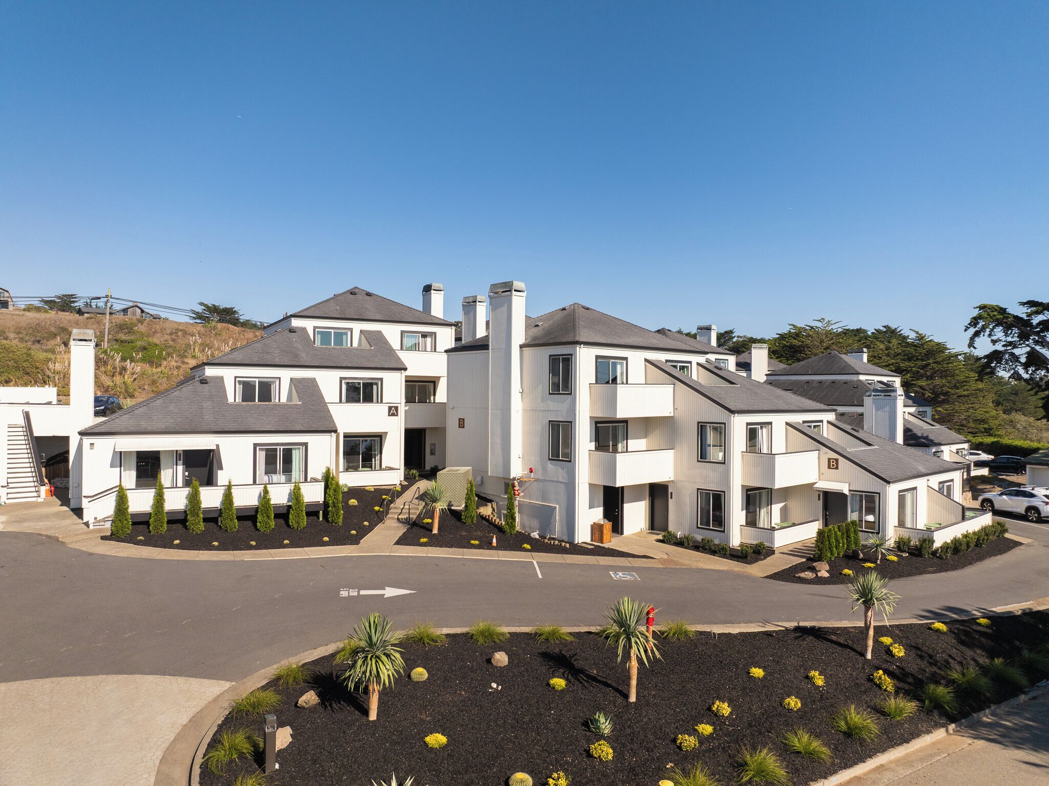 Um edifício residencial moderno com vários andares, entrada coberta e jardins ajardinados.