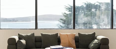 A modern living room with a sofa, a coffee table, and large windows overlooking a body of water.