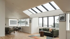 Ein geräumiges Wohnzimmer mit hoher Decke, Dachfenster, großen Fenstern, einem grünen Sofa, einem Schaukelstuhl und einem Couchtisch.
