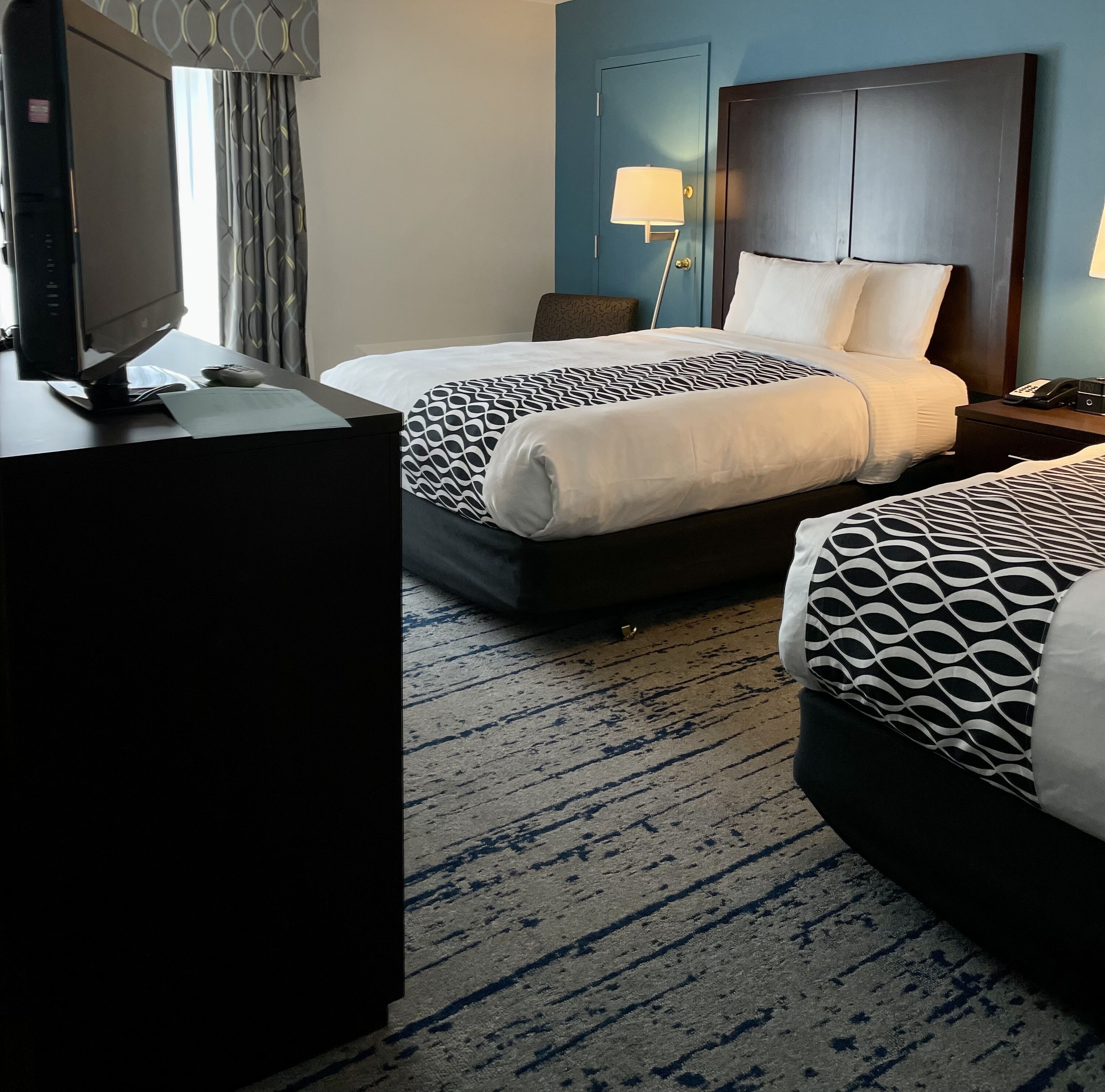 A hotel room with two beds, a desk with a computer, and a lamp.