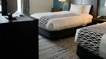 A hotel room with two beds, a desk with a computer, and a lamp.