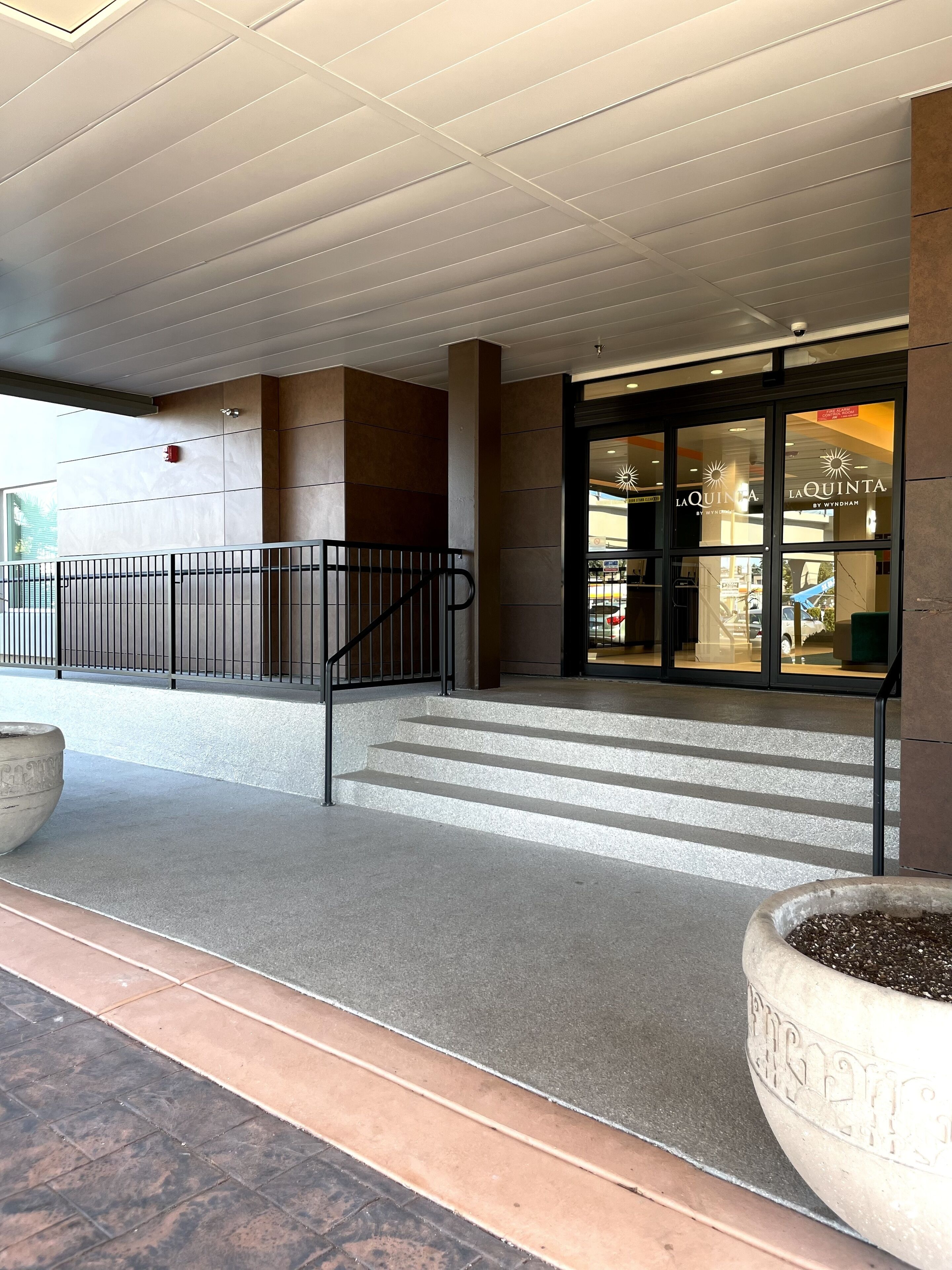 A hotel entrance with a modern design, featuring a glass facade, a staircase leading to the entrance, and a concrete planter with a sign.