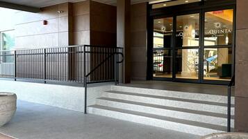 A hotel entrance with a modern design, featuring a glass facade, a staircase leading to the entrance, and a concrete planter with a sign.