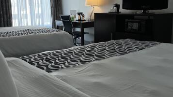 A hotel room with two beds, a desk, a chair, a TV, and a lamp.