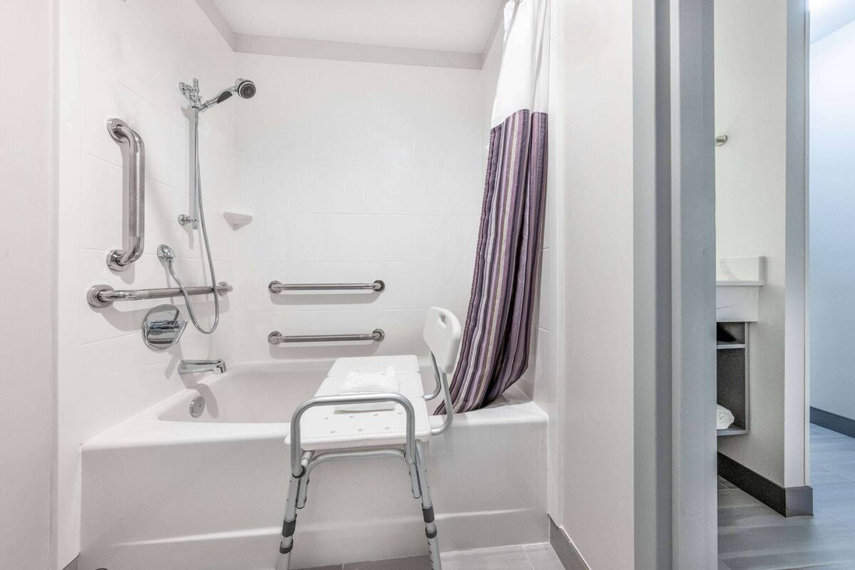 A modern bathroom with a bathtub, shower, and grab bars.