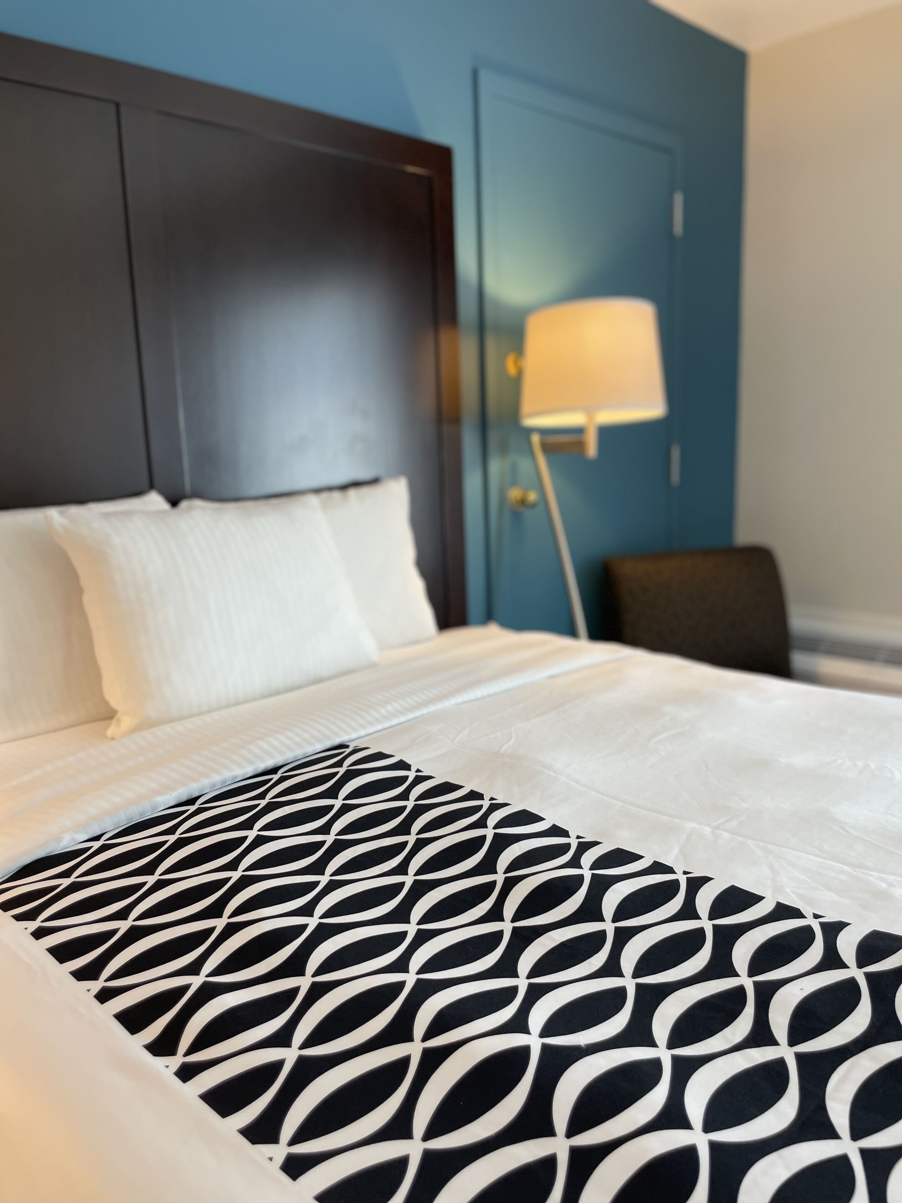 A neatly made bed with a patterned bedspread, a dark headboard, and a lamp beside the bed.