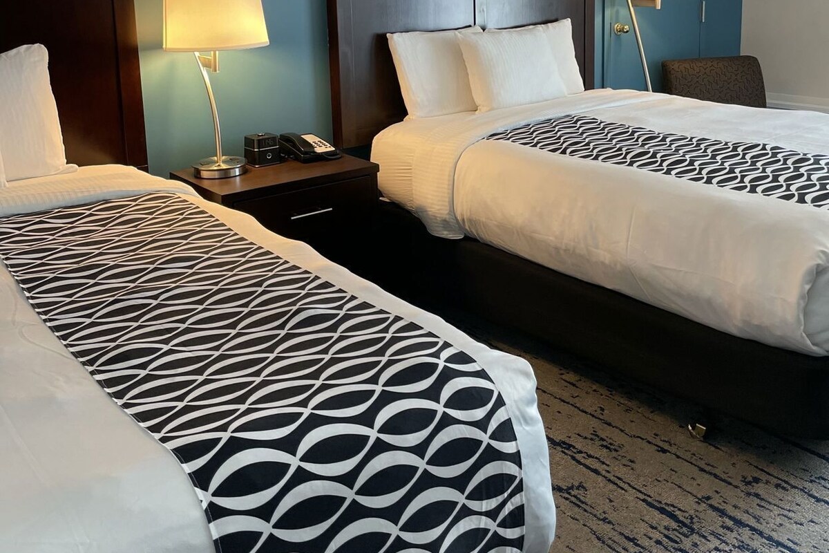 A hotel room with two beds, a nightstand with a lamp, a telephone, and a door with a mirror.