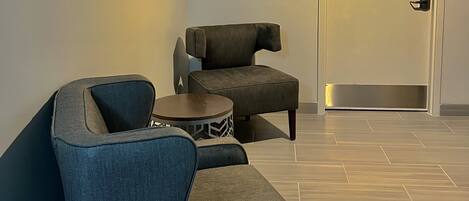 A modern room with a blue armchair, a smaller armchair, and a round side table. A door with a handle is visible in the background.
