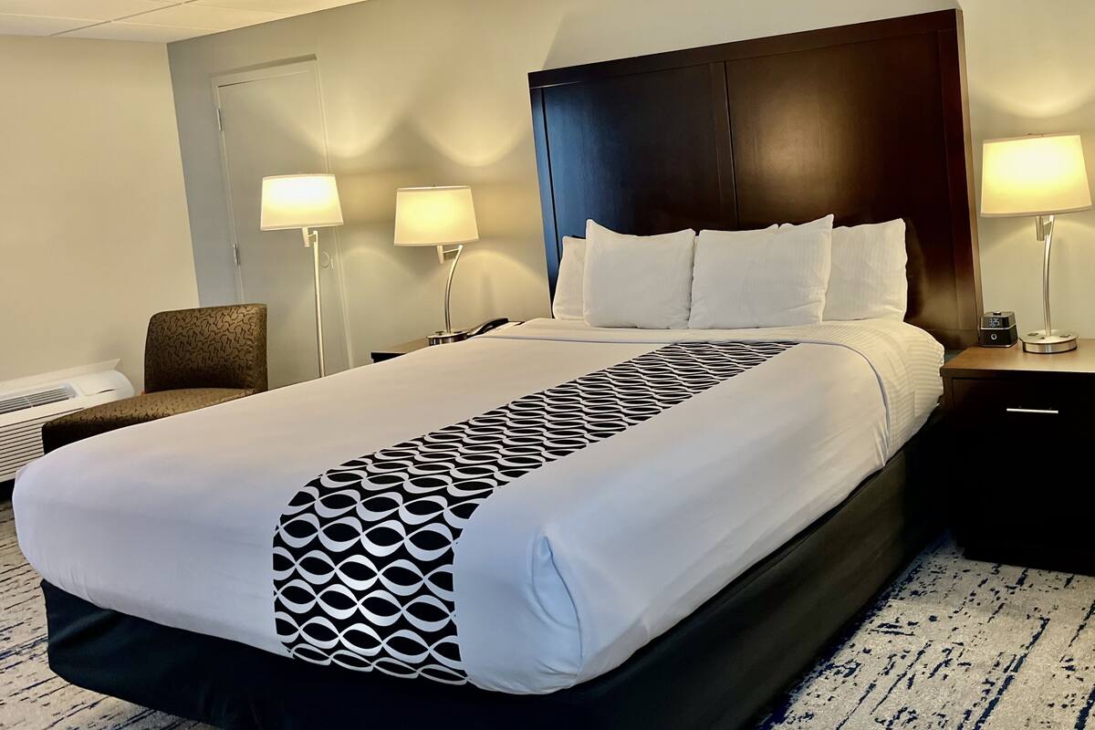 A hotel room with a large bed, two bedside lamps, a nightstand, and a chair.