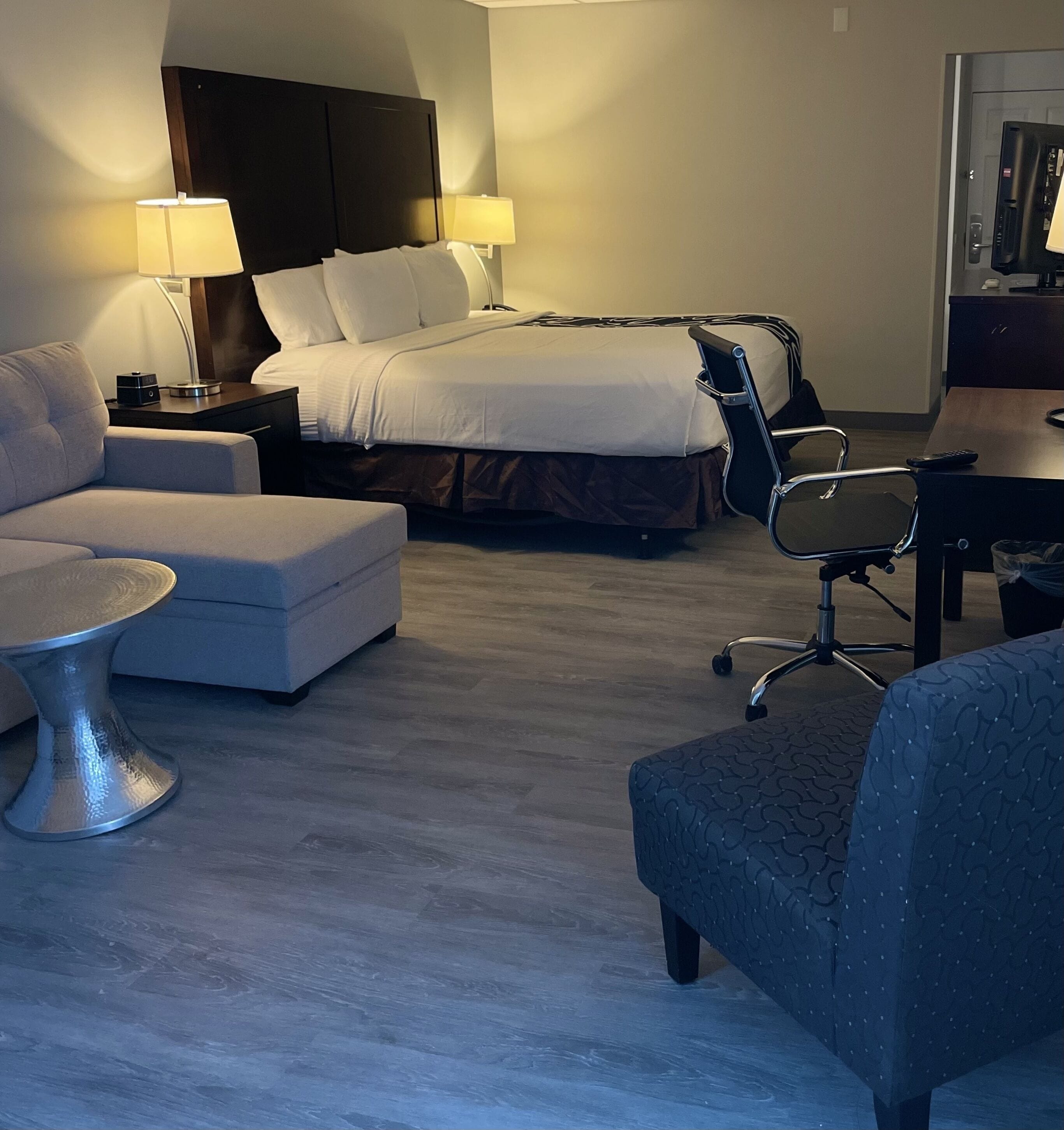 A hotel room with a bed, two bedside tables with lamps, a sofa, a chair, and a small table.
