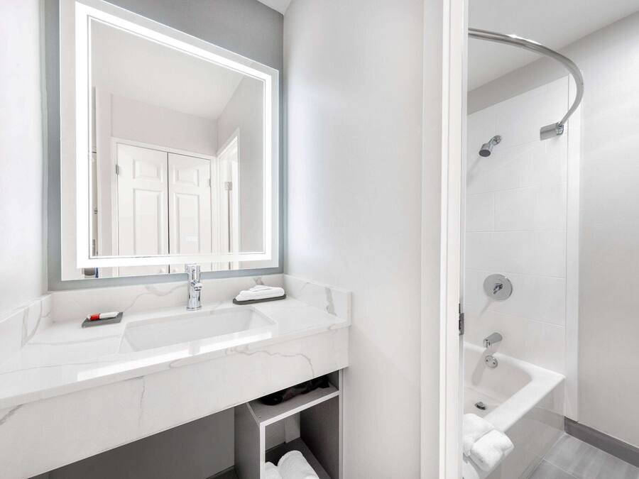 A modern bathroom with a white marble sink, a large mirror, and a shower area.