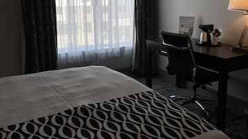 Habitación de hotel con una cama grande, un escritorio con una silla, una lámpara y una ventana con cortinas.