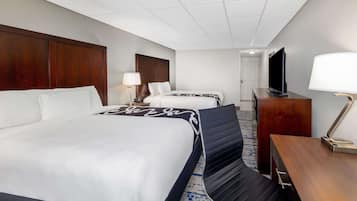 Habitación de hotel con una cama grande, una cama más pequeña, un escritorio con lámpara, televisión y armario.