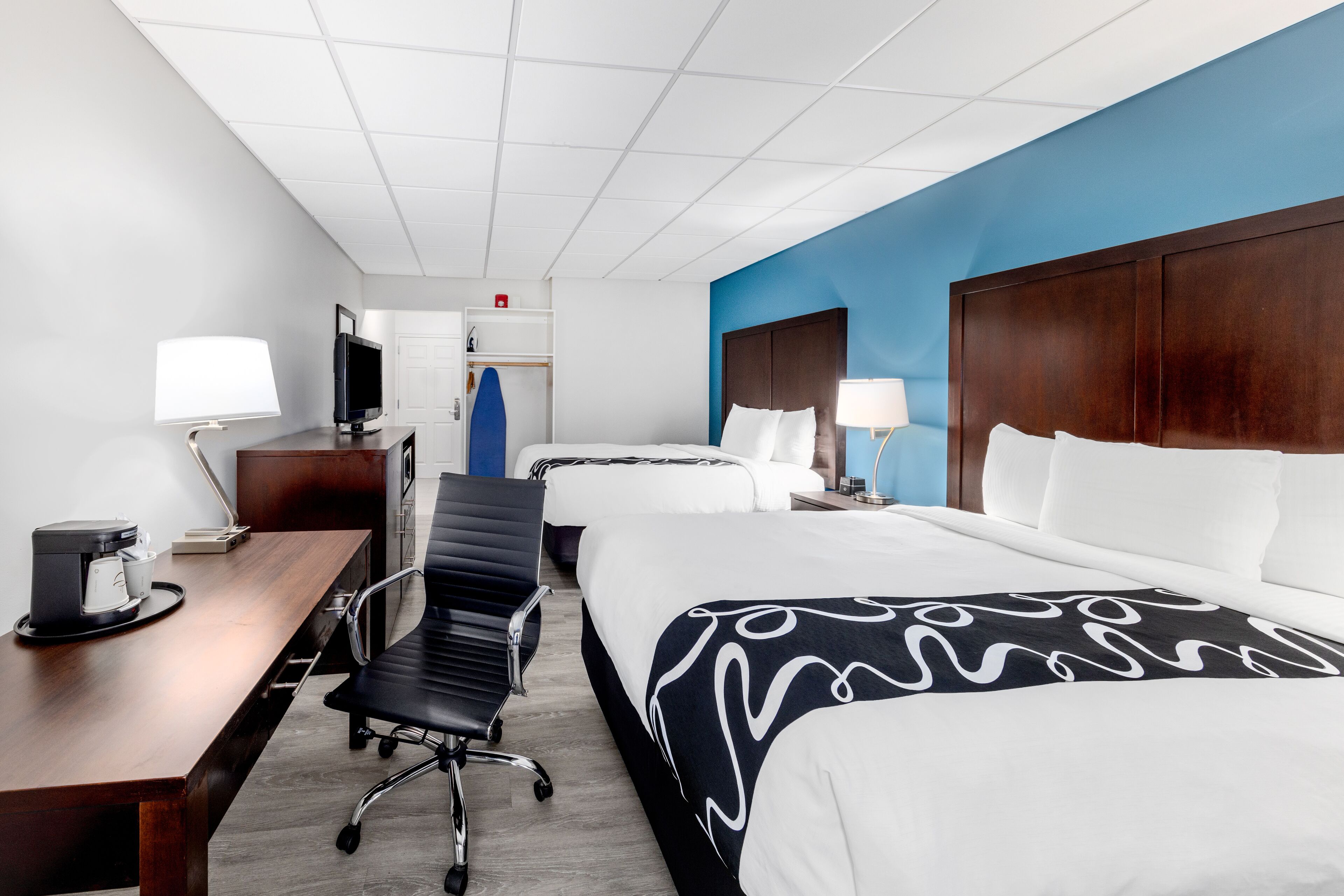 A hotel room with a large bed, a desk with a lamp, a chair, and a television.