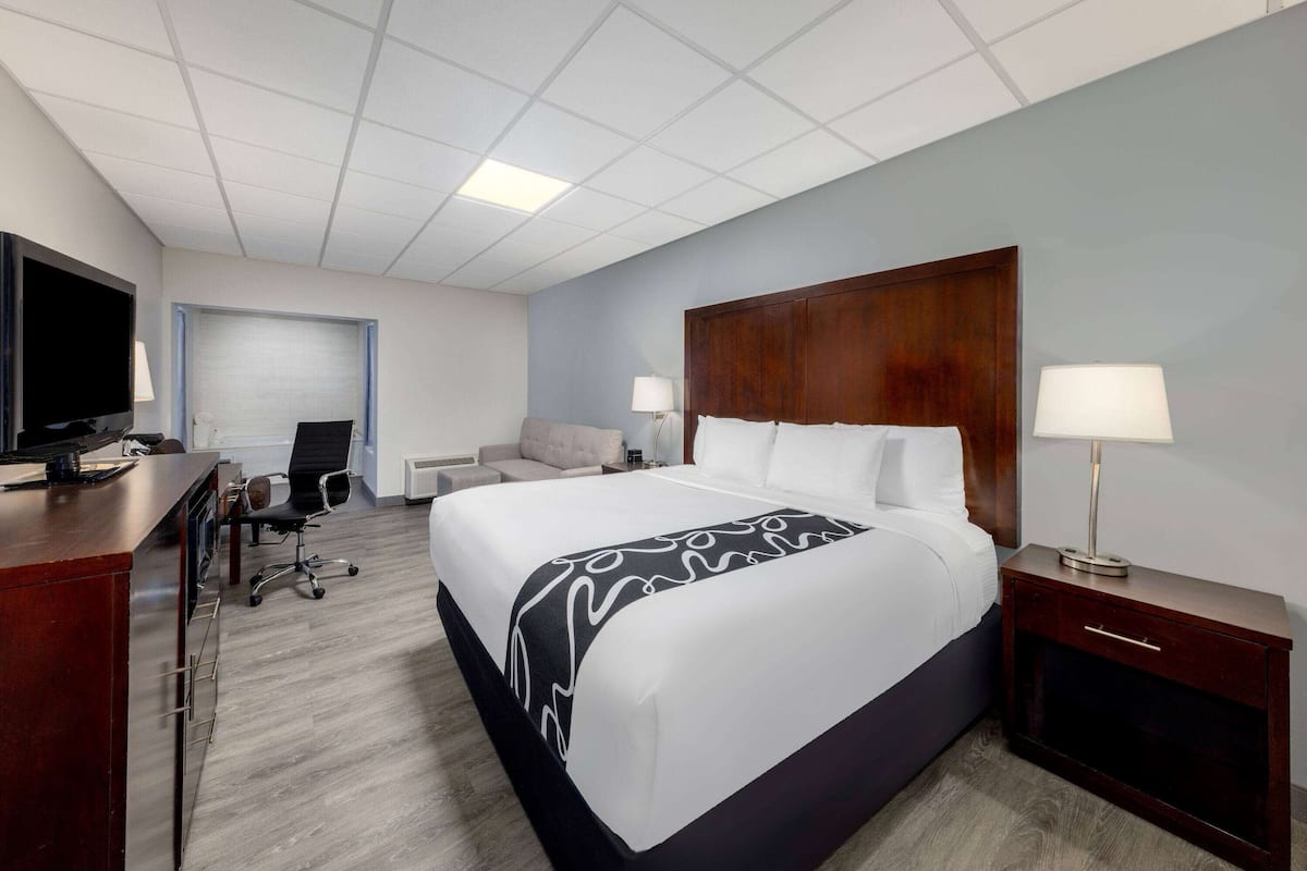 A hotel room with a large bed, a desk with a TV, a chair, a sofa, and two bedside tables with lamps.