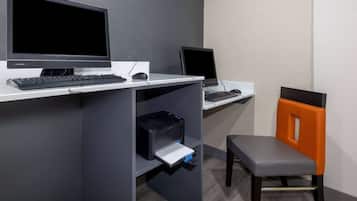 Un espacio de oficina moderno con dos escritorios, cada uno con monitor, teclado y ratón. Hay una impresora en el escritorio de la izquierda, y una silla con respaldo naranja frente al escritorio de la derecha.