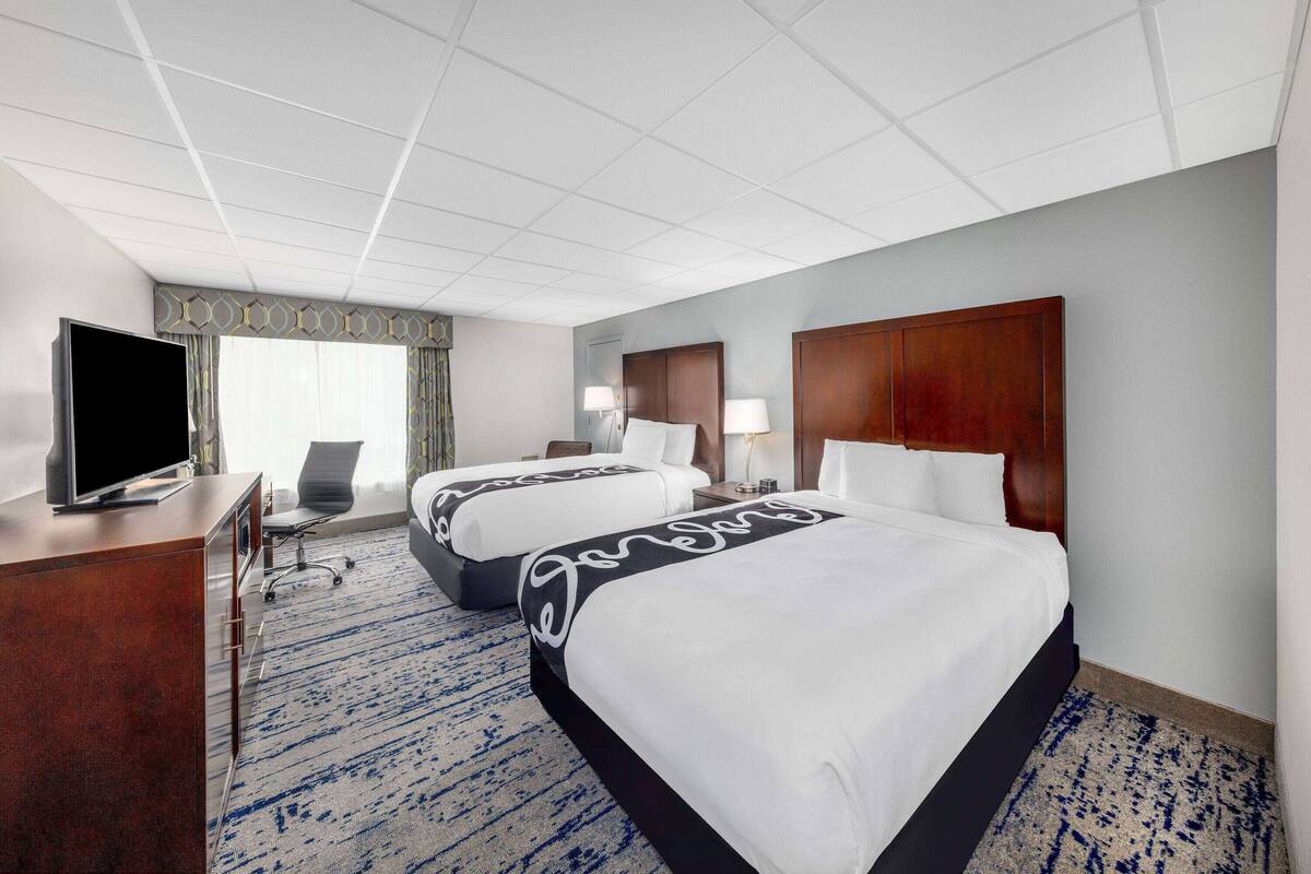 A hotel room with two beds, a TV, a desk, and a window with curtains.