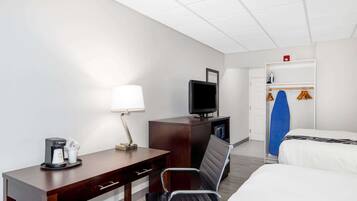 A hotel room with a bed, a desk with a lamp, a television, a coffee maker, and a wardrobe with a surfboard.