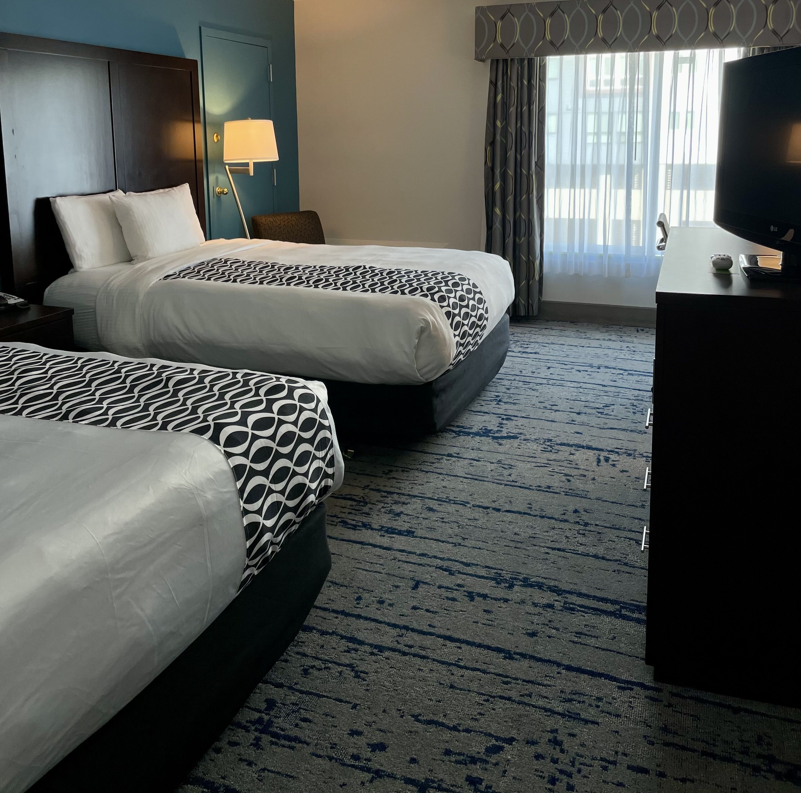 Quarto de hotel com duas camas, uma mesa, uma televisão e um abajur.
