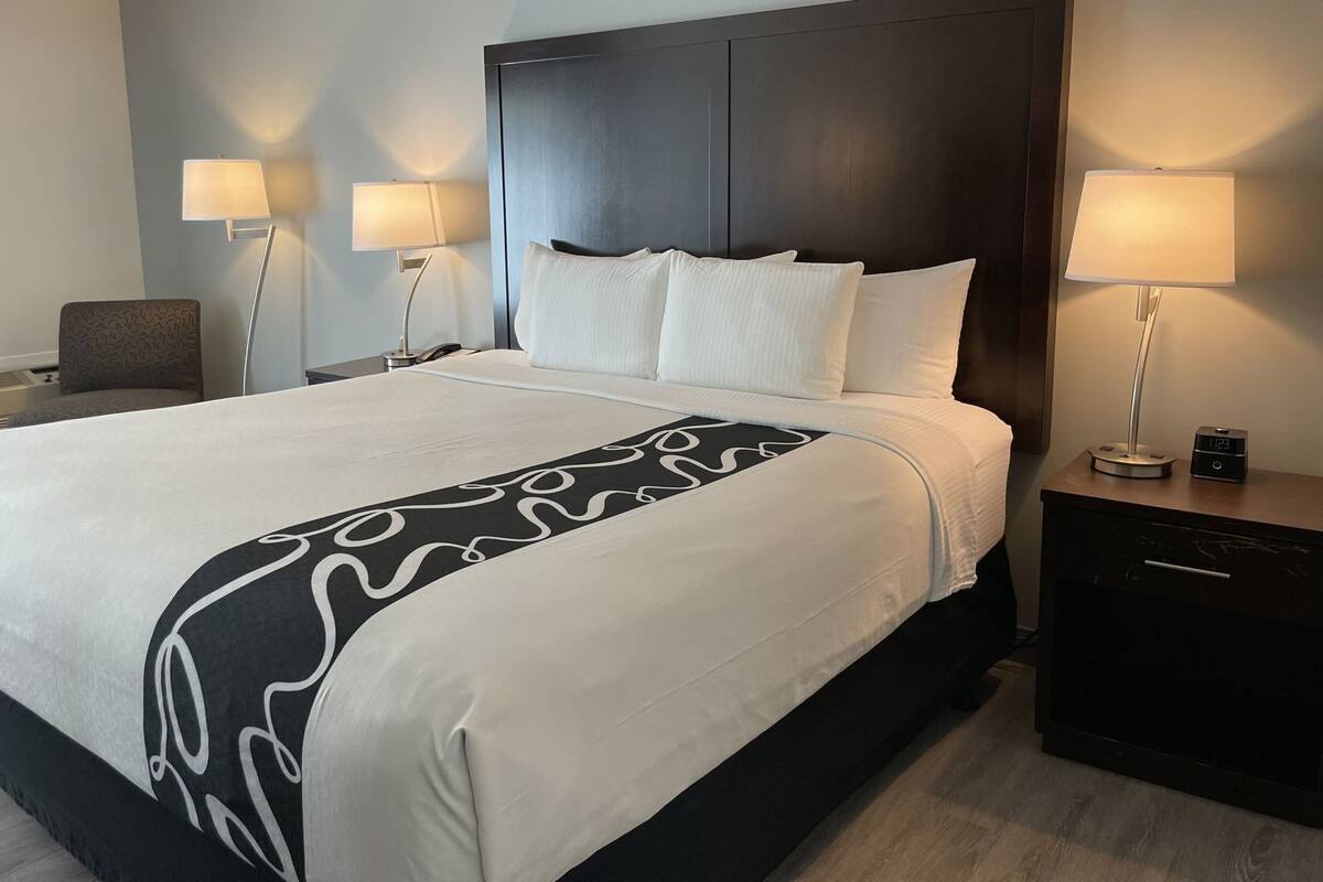 A hotel room with a large bed, two bedside lamps, a nightstand with a clock, and a chair.