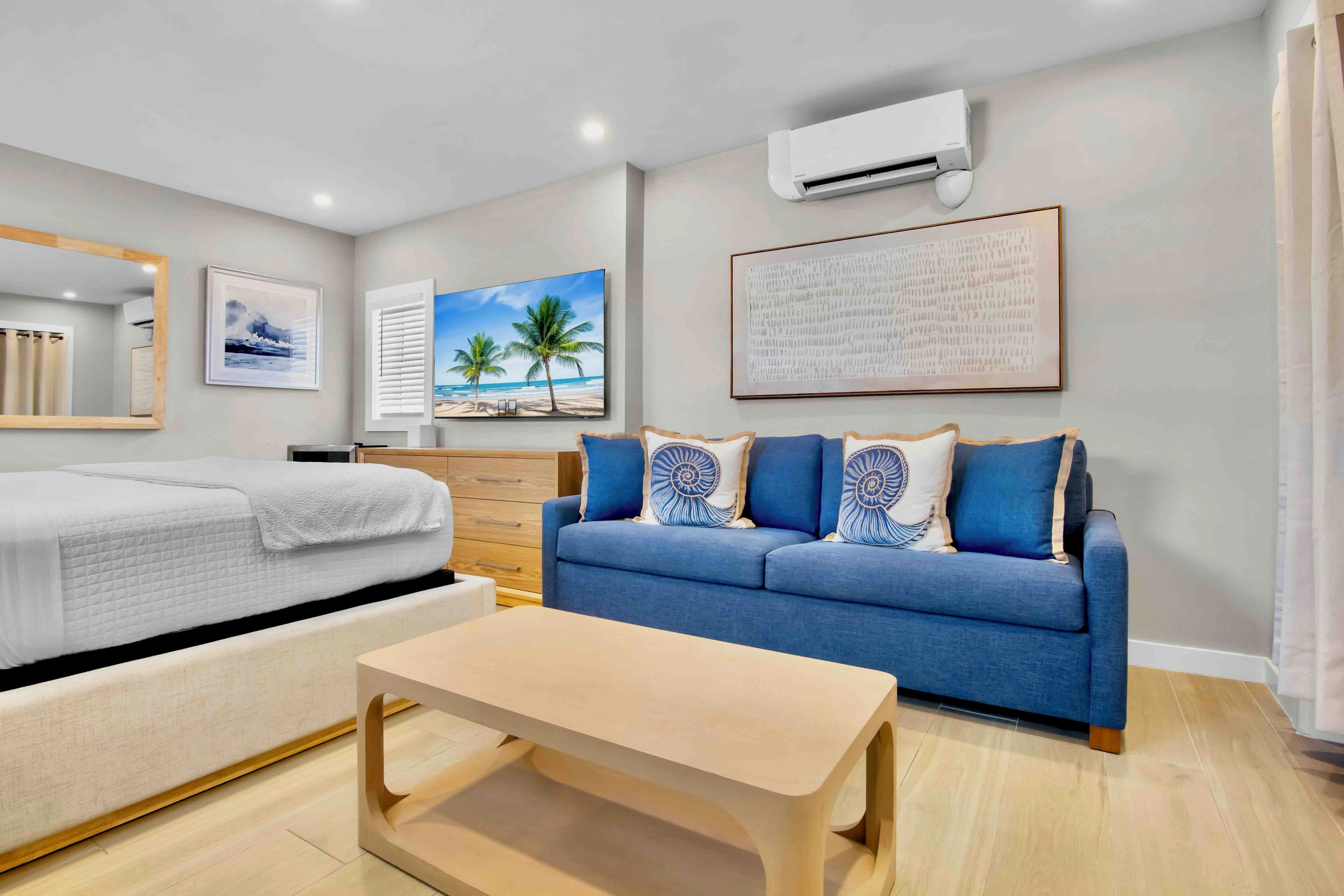A modern hotel room with a bed, a sofa, a coffee table, and a large window.