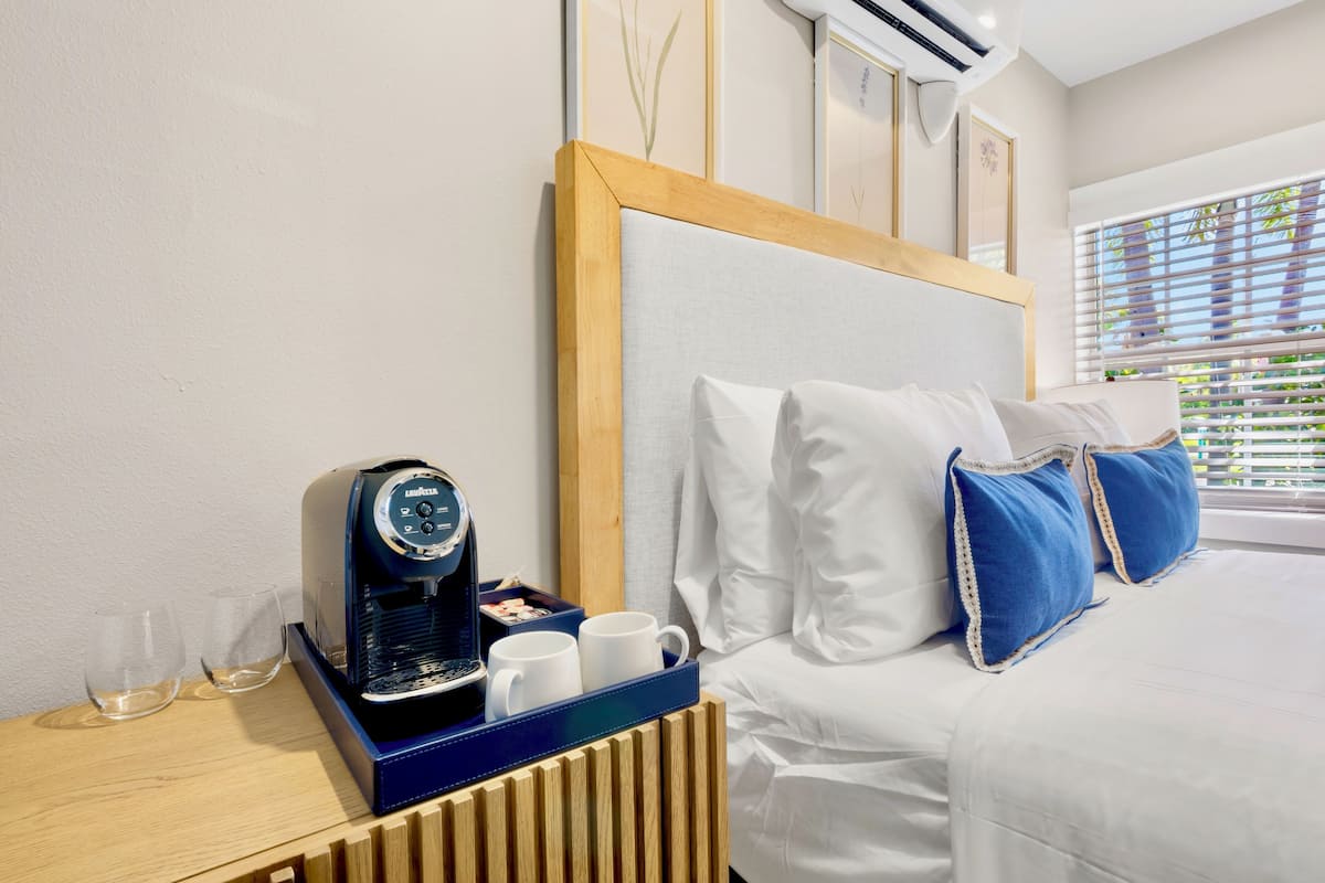 A hotel room with a bed, a coffee machine, two glasses, and a tray with two cups.