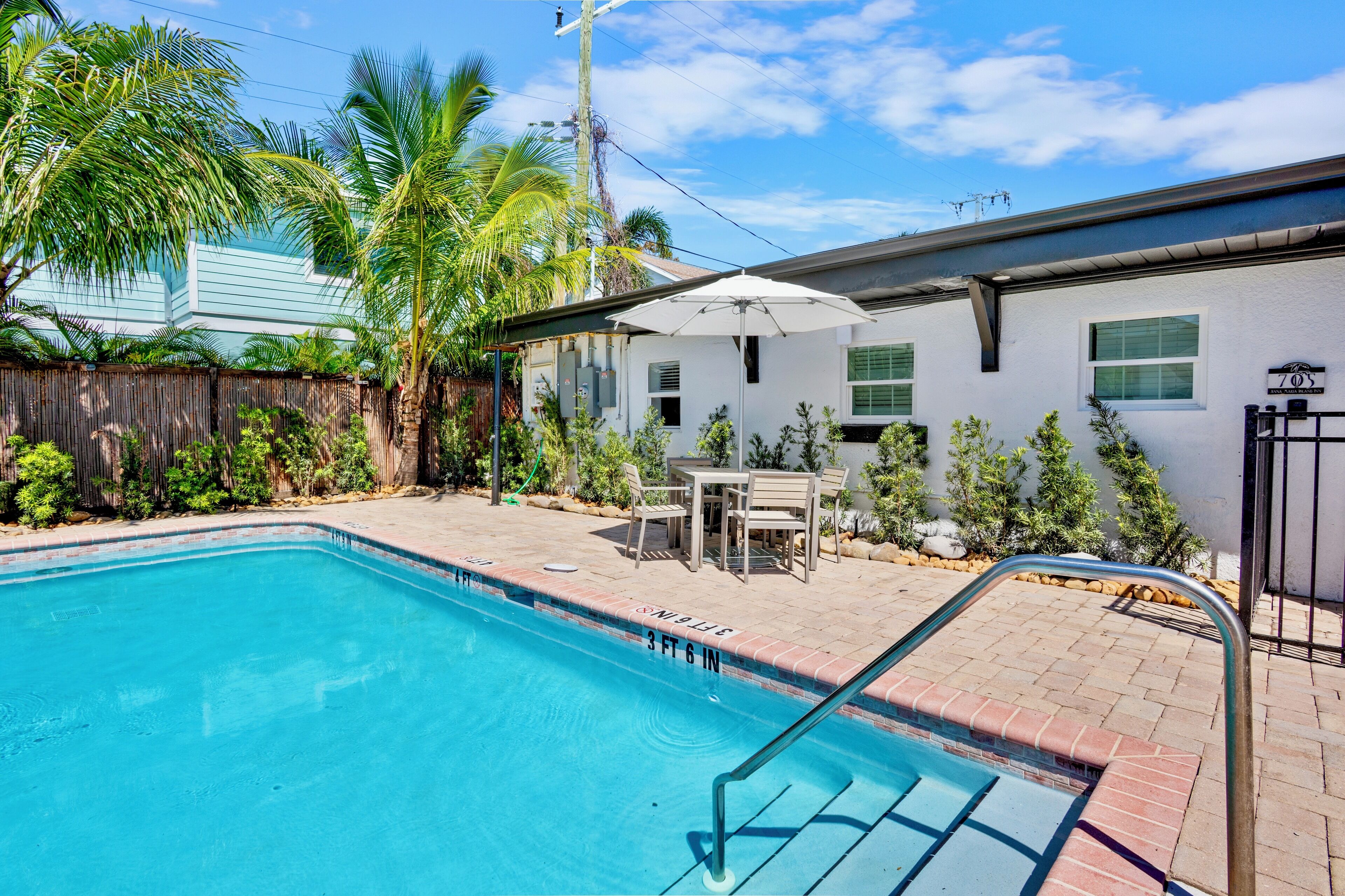 A swimming pool with a 3 ft 6 in depth, surrounded by a wooden fence, palm trees, and a patio area with outdoor furniture.