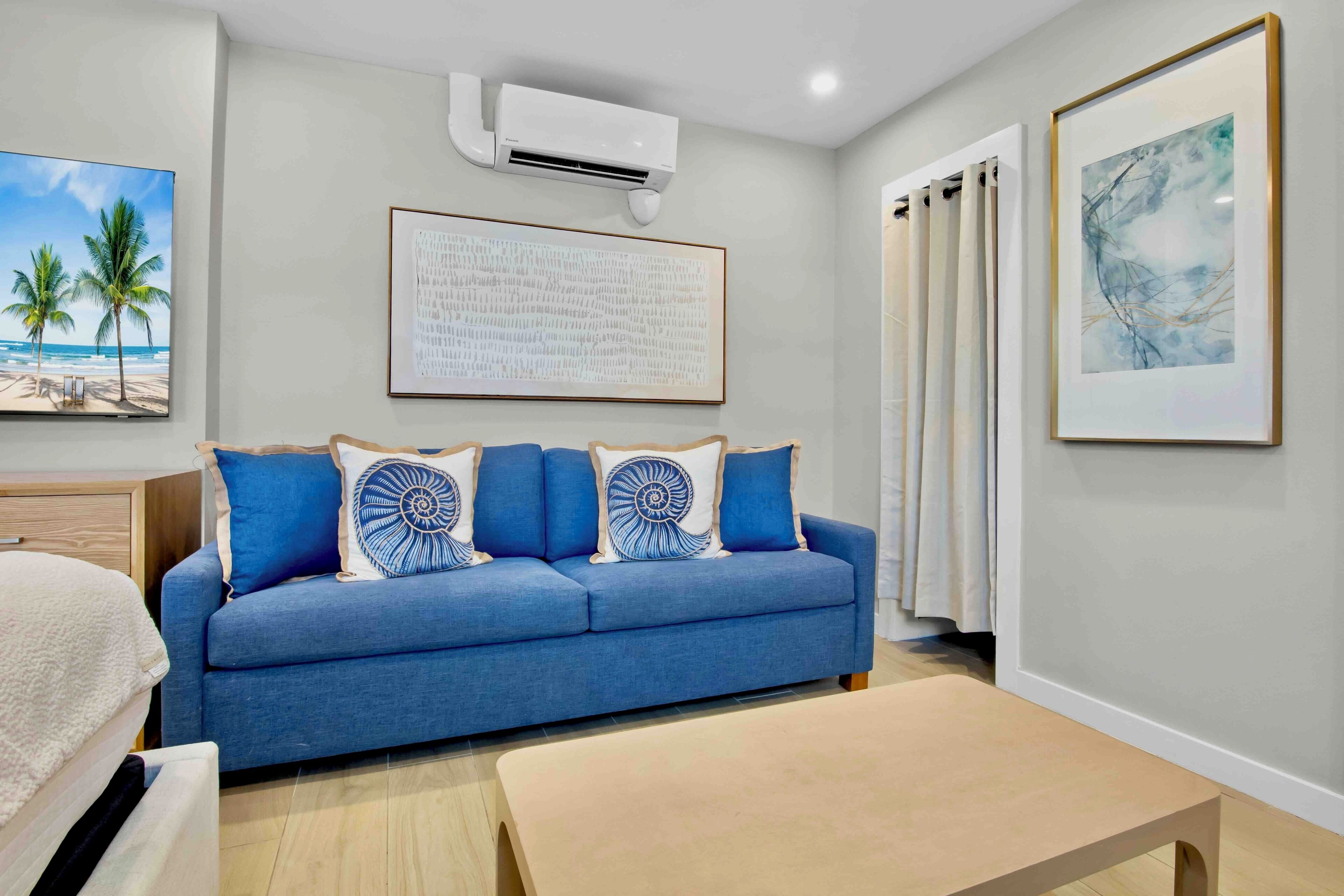 A modern room with a blue sofa, a wooden coffee table, and a bed with a white headboard.
