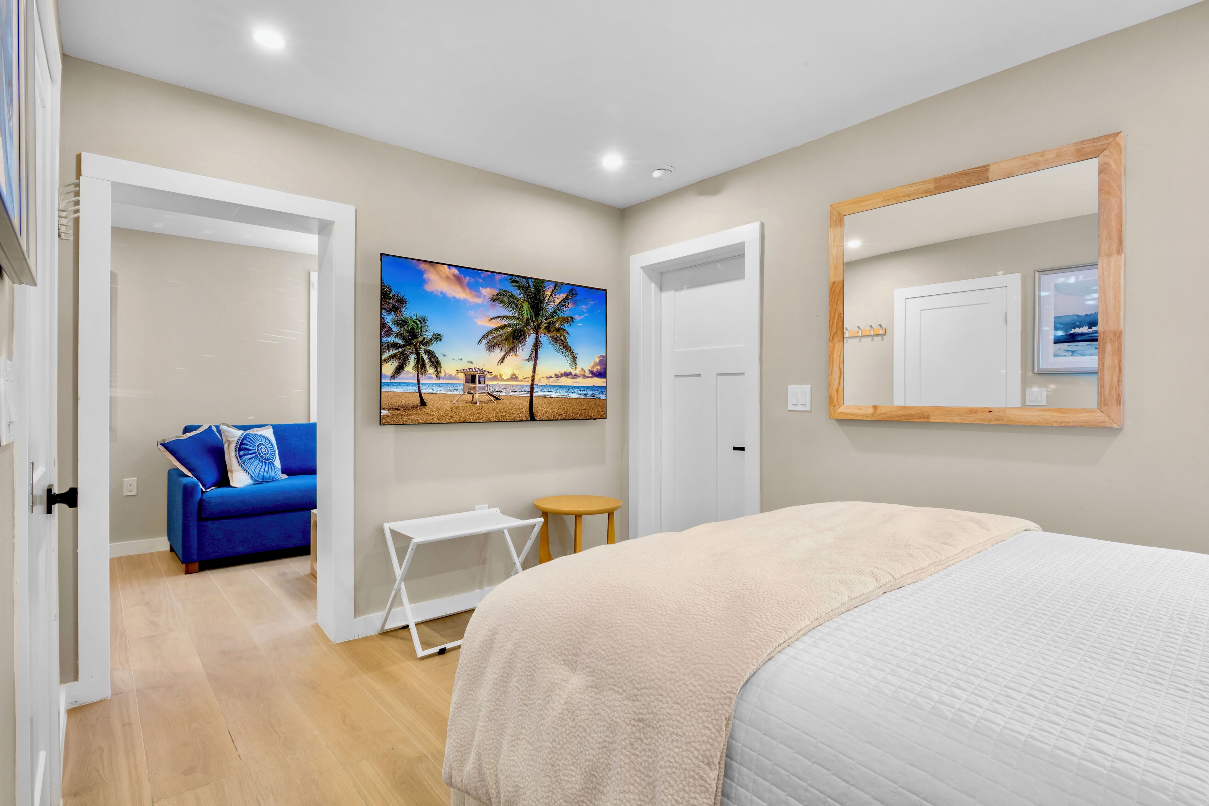 A bedroom with a bed, a blue sofa, a small table, and a painting of a beach scene.