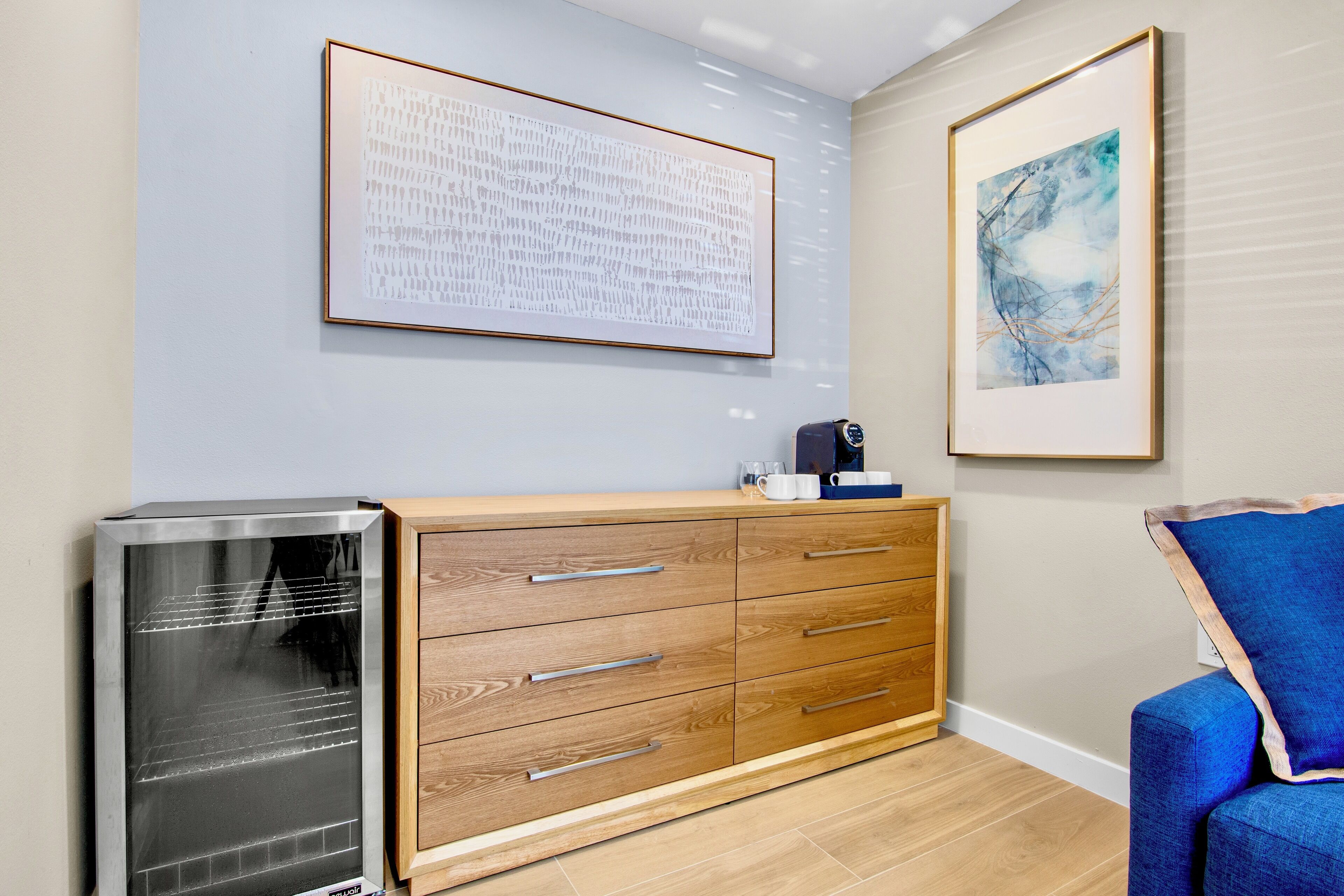 A modern room with a wooden cabinet, a refrigerator, and two framed artworks on the wall.