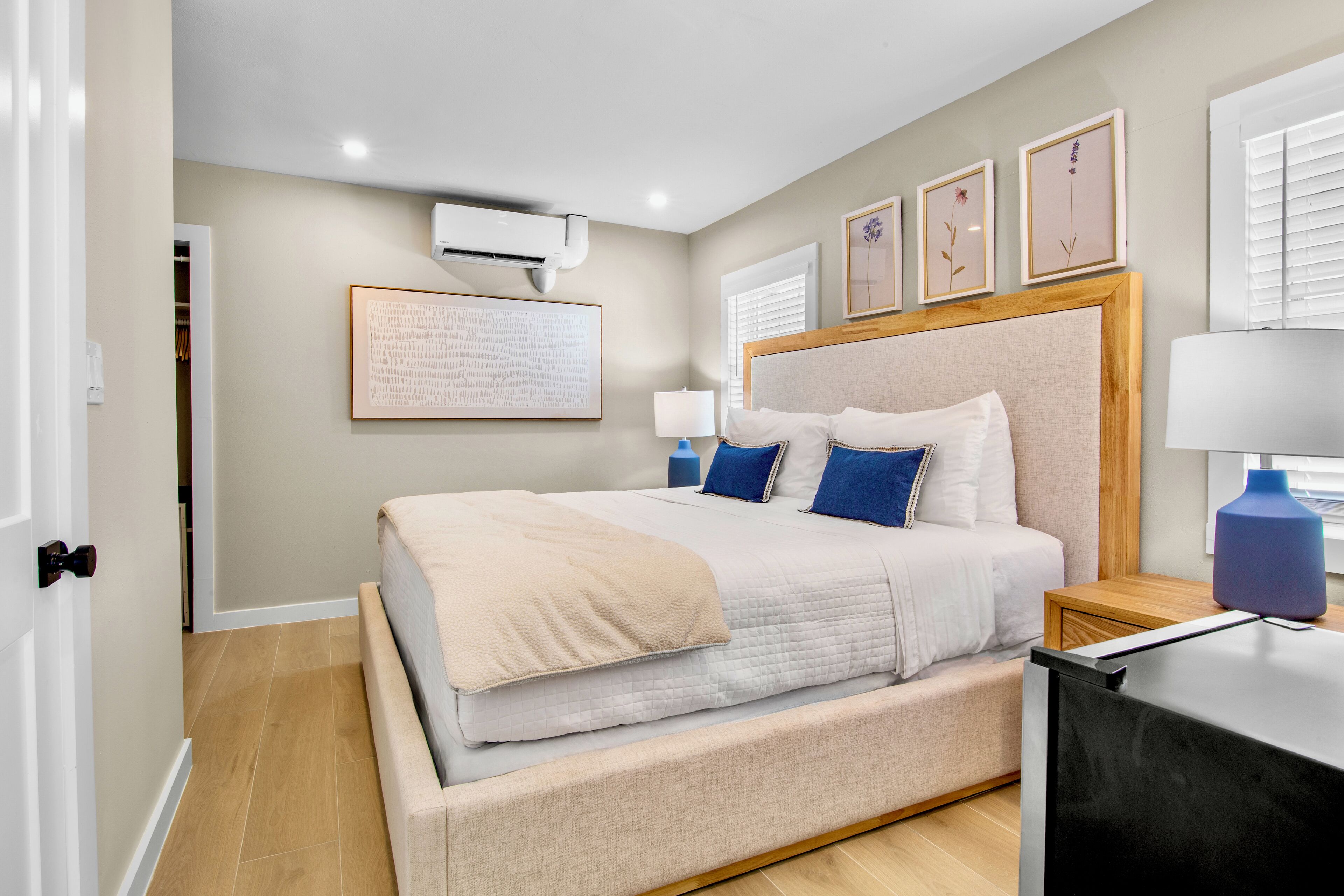 A bedroom with a large bed, a bedside table, a lamp, and framed artwork on the wall.