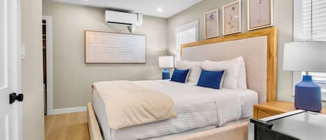 A bedroom with a large bed, a bedside table, a lamp, and framed artwork on the wall.